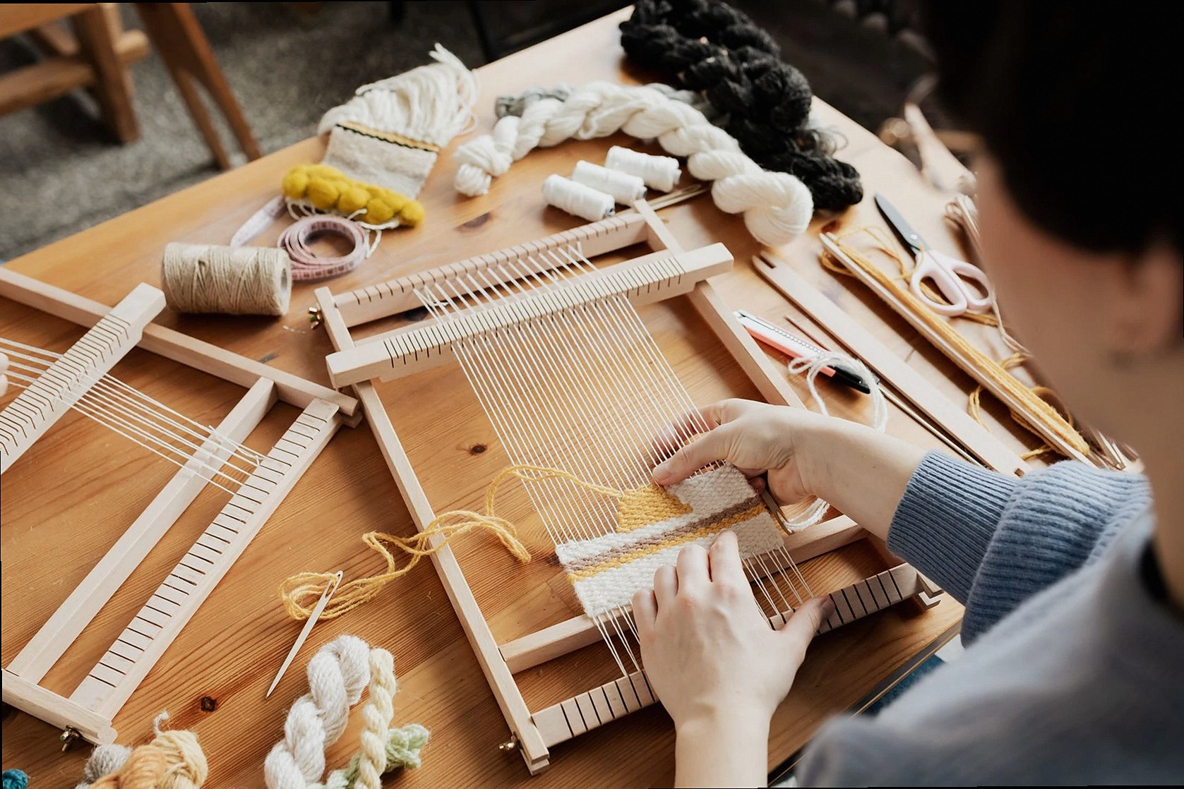 Una persona tejiendo textiles con un telar de madera manual, mostrando creatividad y artesanía.